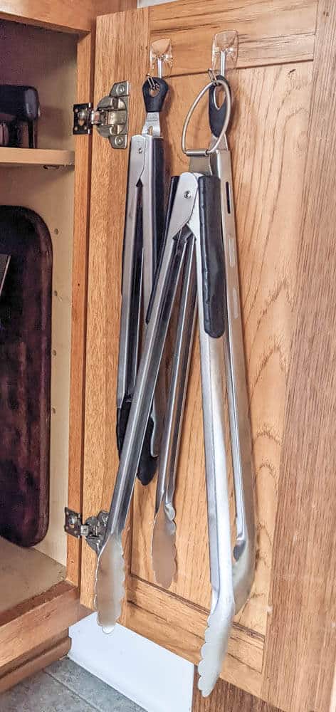 kitchen tongs hung on hooks on cabinet door