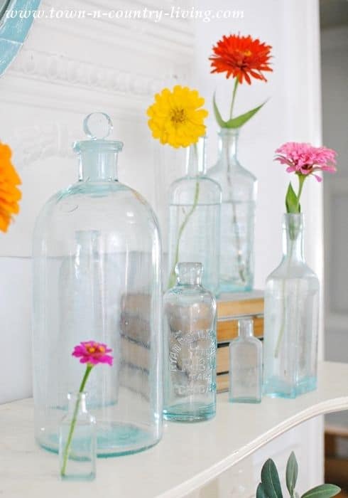 Zinnias in vintage glass bottles make perfect summer mantel decor.