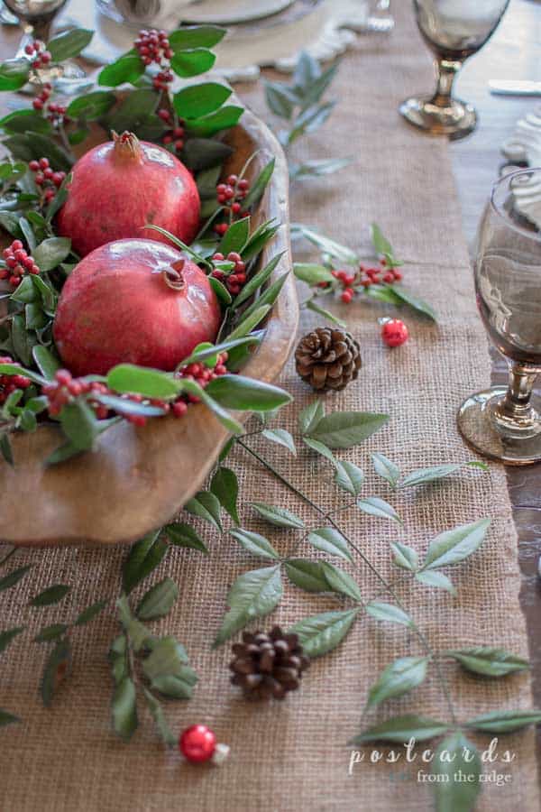 Christmas table with burlap runner, wooden dough bowl with pomegranites, and holly