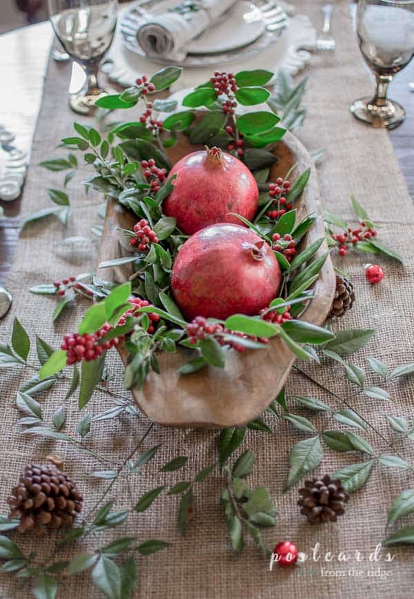 Christmas table centerpiece with pomegranites and holly in a wooden dough bowl