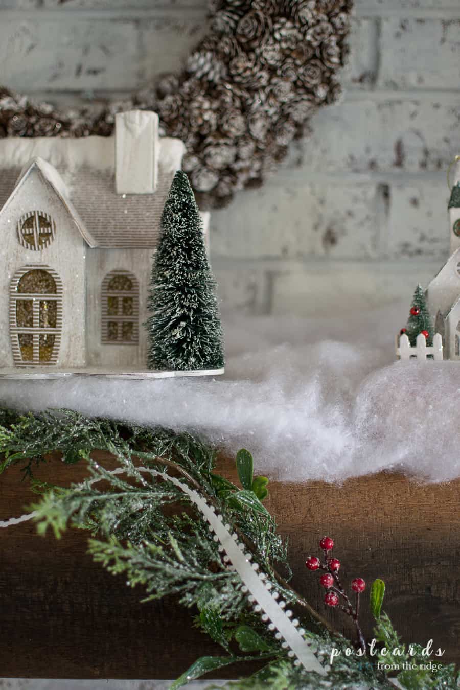 Snowy paper house with bottle brush tree on a farmhouse Christmas mantel