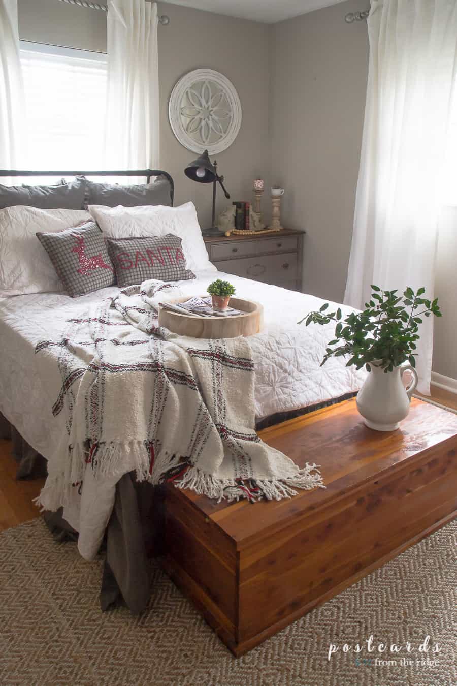 bed with white quilt, black headboard, white curtains, and woven rug