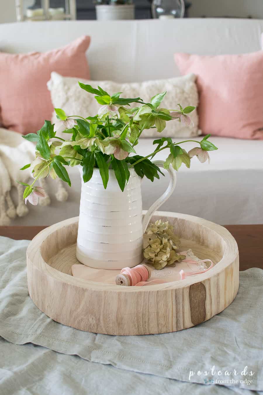 Lenten roses in a white pitcher on a round wood tray