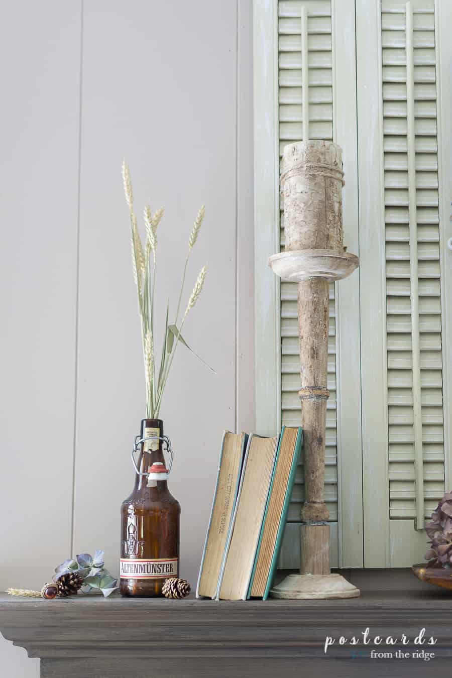 old books and vintage beer bottle with tall wood candlestick on mantel