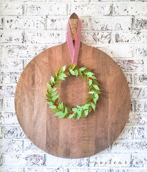 round cutting board with felt holly leaf wreath on white brick wall