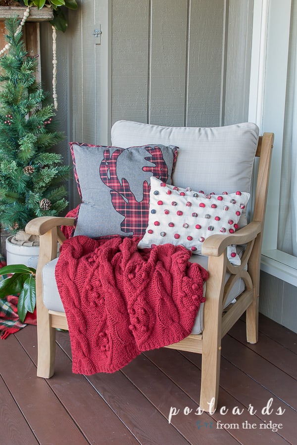 outdoor teak chair with red cable knit throw blanket and holiday pillows
