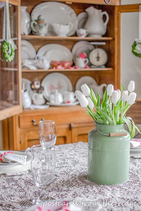 white tulips in a green milk can on a vintage lace tablecloth