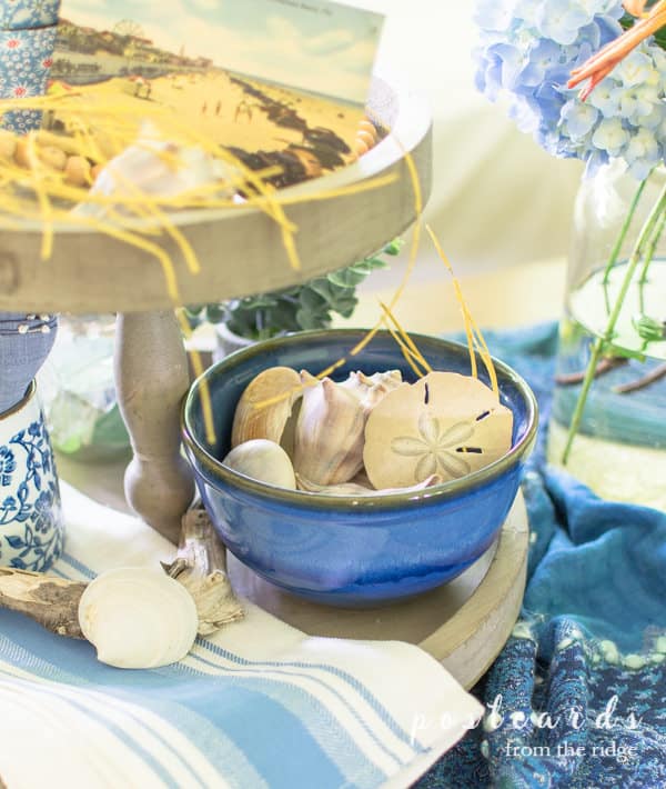 blue pottery bowl with seashells on a wood tiered tray