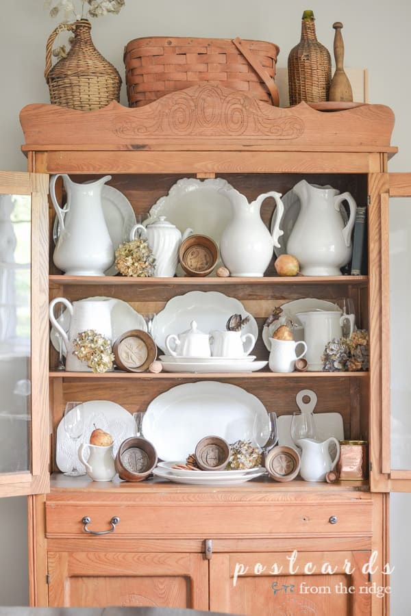 wooden butter molds and white ironstone pitchers and platter in antique oak hutch