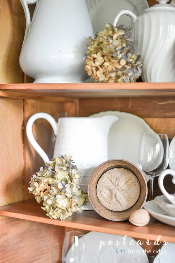 dried hydrangeas, white ironstone, wooden butter molds in antique oak hutch