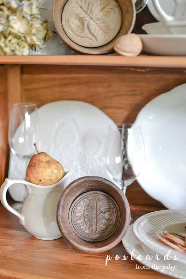 vintage wooden butter mold and white creamer with pear in antique oak hutch