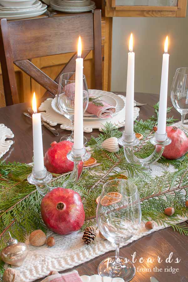 Christmas table with pomegranates, evergreen branches, vintage glass candle holders
