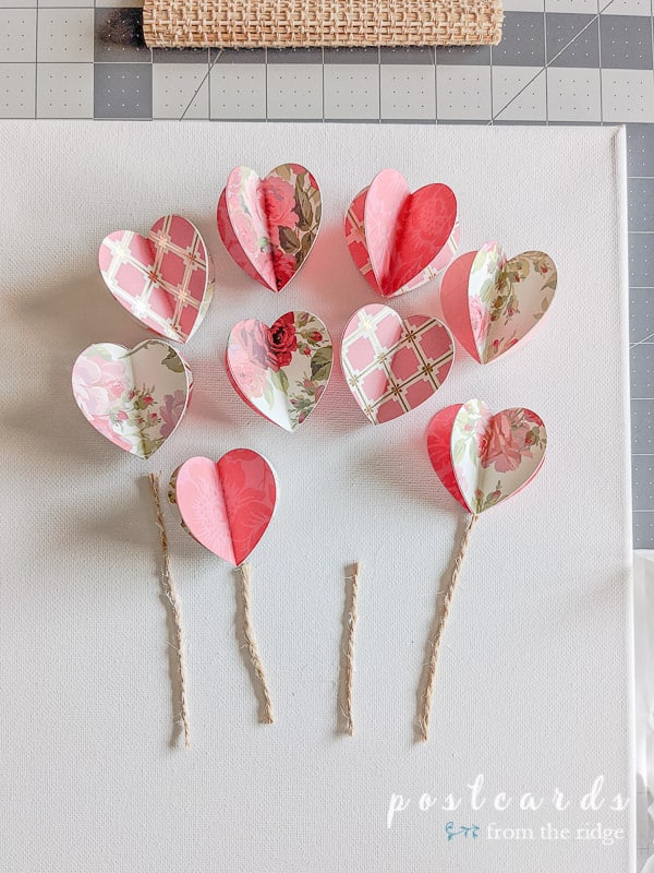 3-d floral paper hearts and pieces of twine on white canvas