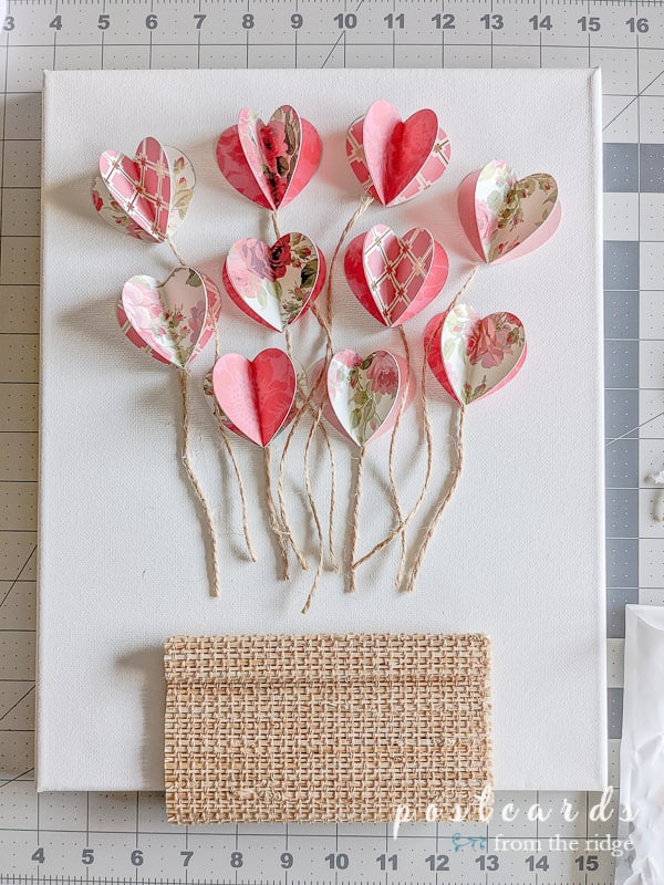 pieces of twine and 3-d paper hearts on white canvas