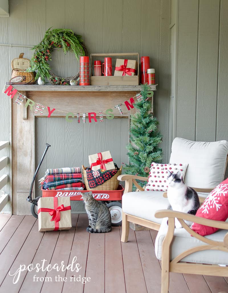 Christmas decor on a covered deck including a red wagon, plaid blankets, and vintage thermoses