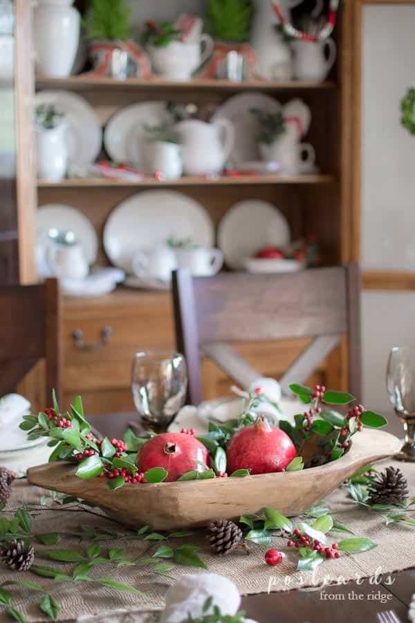 wooden dough bowl with pomegranates and holly clippings as centerpiece on a Christmas table