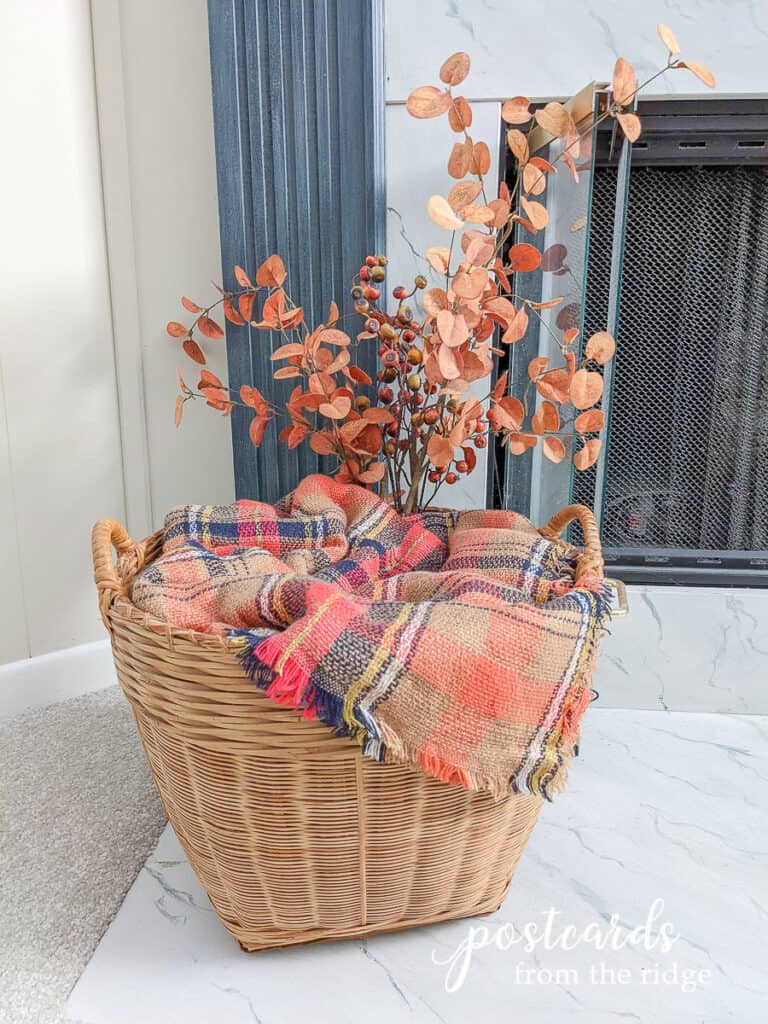 large wicker basket with orange plaid blanket scarf and fall branches