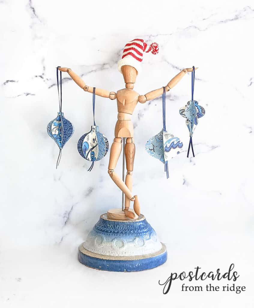 blue and white paper 3D ornaments hanging from a wooden human art form