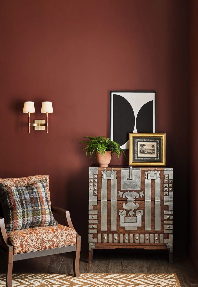 Sherwin Williams Red Barn SW 7591 walls with brass wall sconce and upholstere arm chair with detailed dresser and modern art