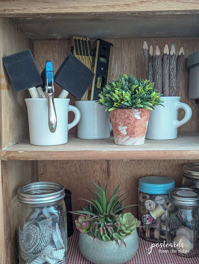 craft supplies organized with vintage ironstone coffee mugs